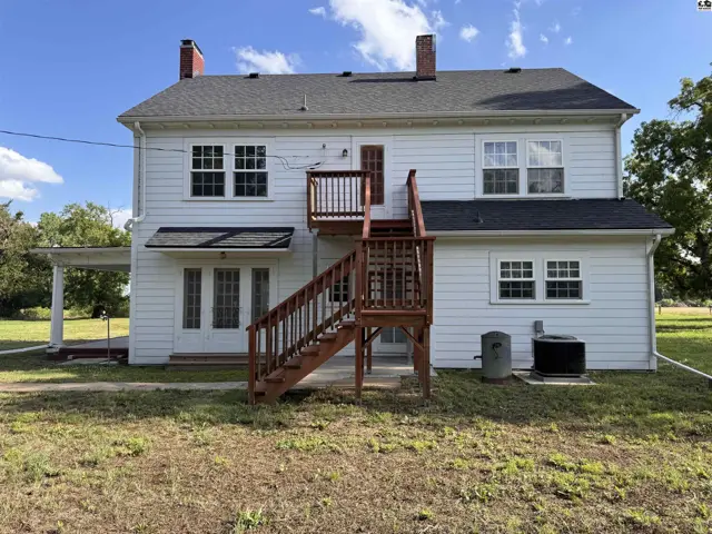 White clapboard house with dark roof, featuring a prominent wooden deck and staircase.