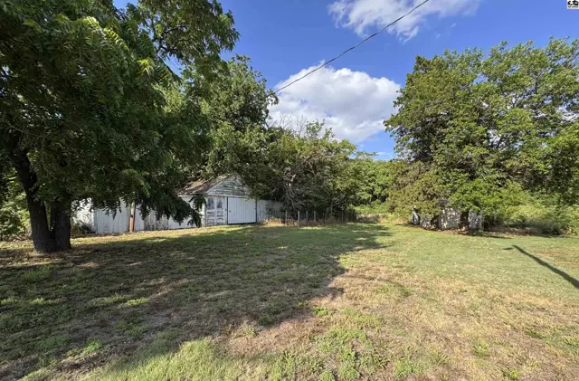 Exterior view of a white, weathered barn surrounded by mature trees and a grassy yard.