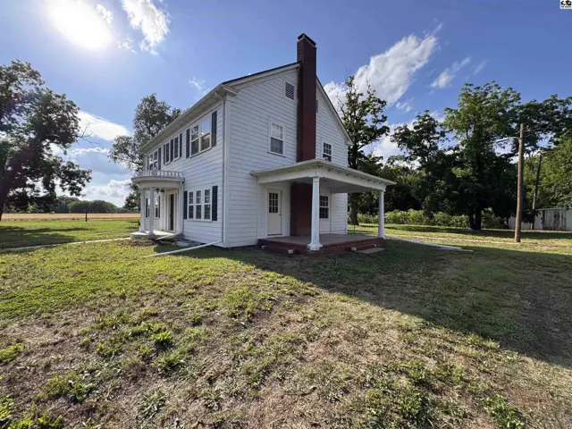 White clapboard farmhouse with a red brick chimney, covered porch, and dark shutters.