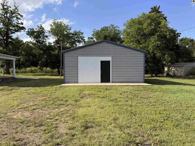 Gray metal garage with a large white roll-up door and a black entry door on a concrete pad.