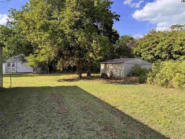 Spacious backyard with mature trees, a white shed, and a light-colored metal outbuilding.