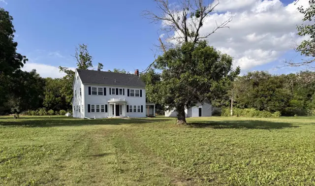 Spacious white colonial home with black shutters and a large green lawn.