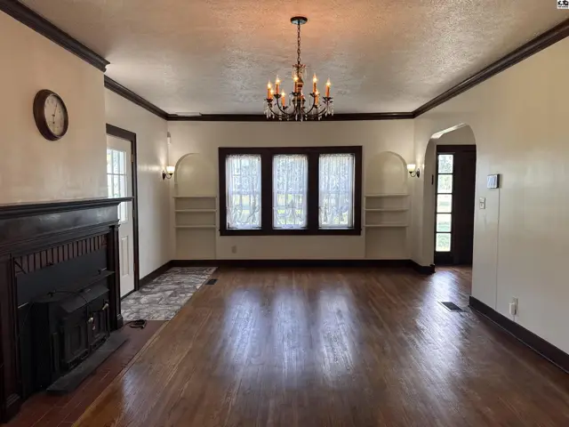 Spacious living room with hardwood floors, fireplace, built-in shelves, and a chandelier.