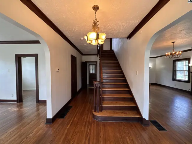 Spacious foyer with hardwood floors, dark wood trim, and a grand staircase leading upstairs.