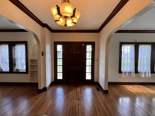 Spacious entryway with dark wood door, gleaming hardwood floors, and arched doorways.