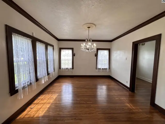 Spacious dining room with hardwood floors, white lace curtains, and a crystal chandelier.