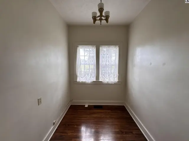 Narrow room with white walls, hardwood floors, and a two-pane window with lace curtains.
