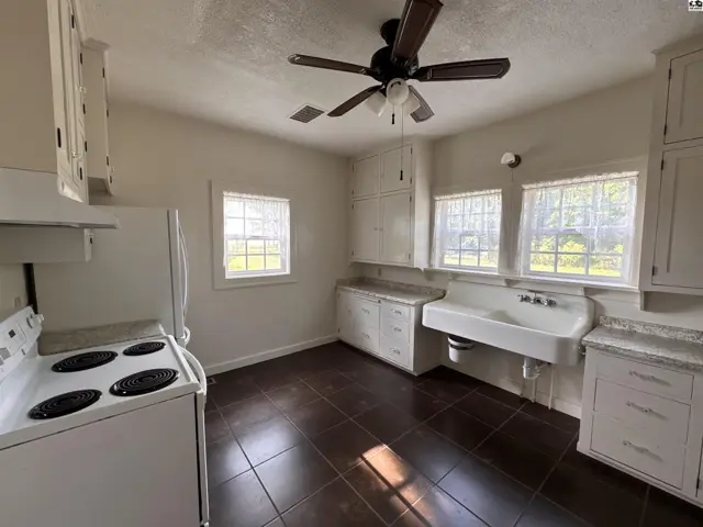 Bright kitchen with white cabinets, a large sink, dark tile floors, and a ceiling fan.