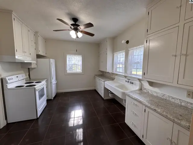 Spacious kitchen with white cabinets, a large farmhouse sink, and dark tile flooring.