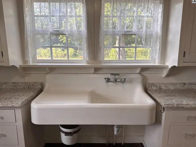 Farmhouse kitchen sink with granite countertops and lace-curtained windows.