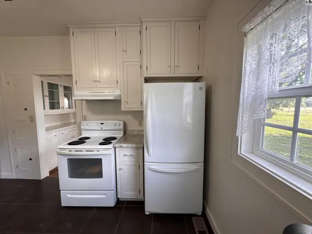 White cabinets and appliances complement a white stove and dark flooring in this compact kitchen.