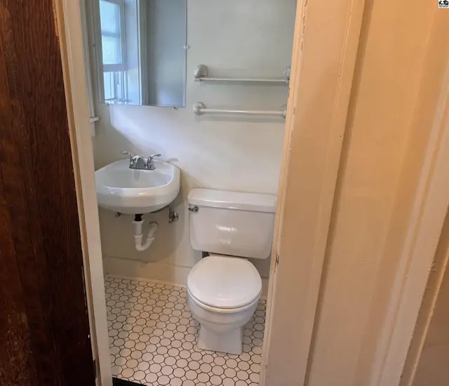 Compact bathroom with a pedestal sink, white toilet, and hexagonal tile flooring.