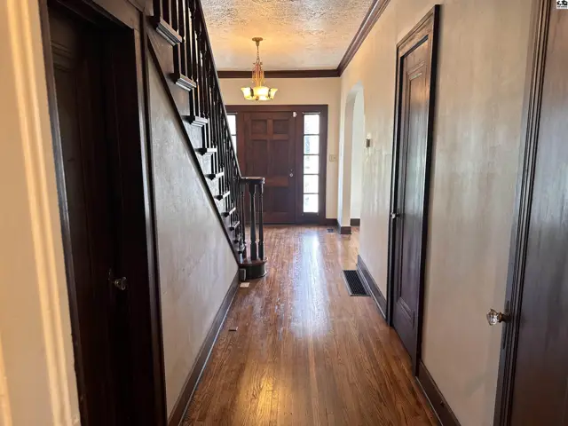 Warm wood floors and dark wood trim highlight this inviting entryway with a grand staircase and chandelier.
