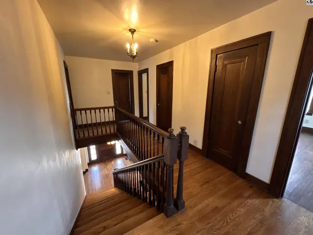 Spacious hallway with rich wood trim, doors, and a grand staircase leading to a lower level.