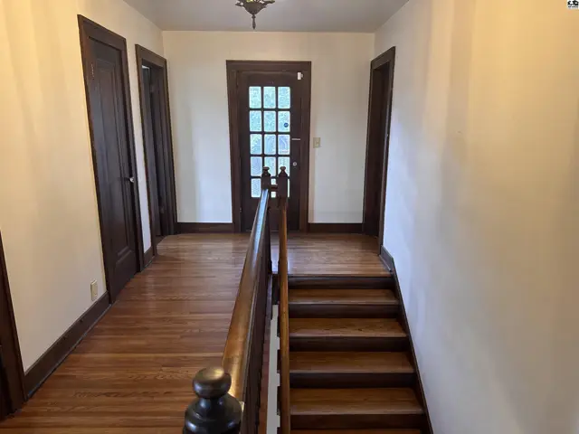 Hallway with hardwood floors, dark wood doors, and a glass-paneled entry door.