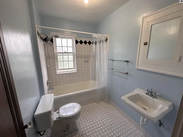 Light blue bathroom with white hexagonal floor tiles, clawfoot tub, and vintage medicine cabinet.