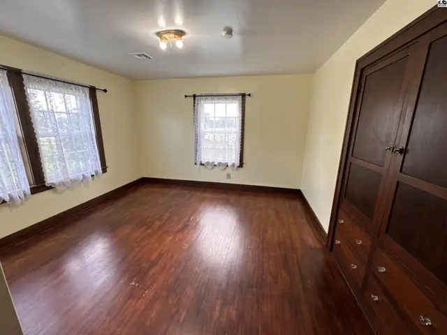 Spacious bedroom with hardwood floors, large windows with lace curtains, and a built-in wooden wardrobe.