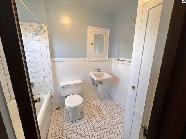 Bright bathroom with white subway tile shower, pedestal sink, and hexagonal floor tiles.