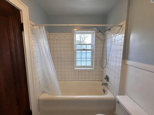 Classic bathroom with white tiled shower surround, bathtub, and a small window.