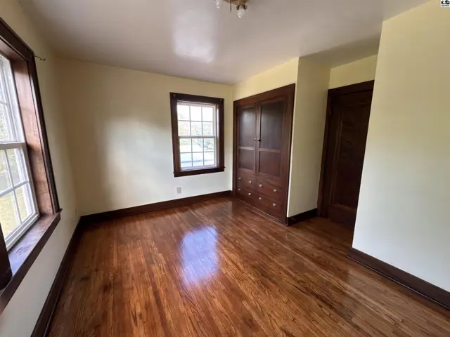 Bedroom with gleaming hardwood floors, large windows, and a built-in wooden closet.