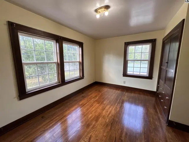 Bright bedroom with polished hardwood floors, large windows, and a dark wood closet.