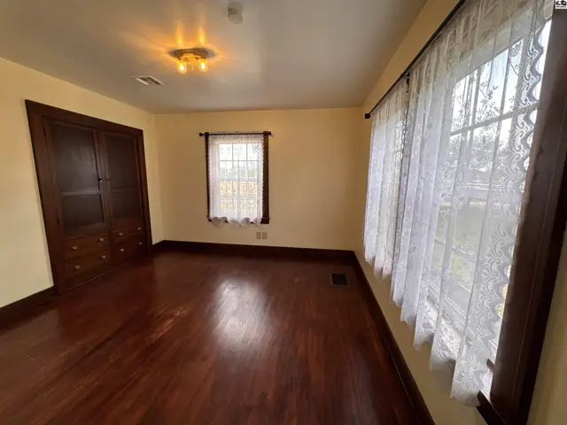 Spacious room with dark wood floors, built-in cabinetry, and large lace-curtained windows.