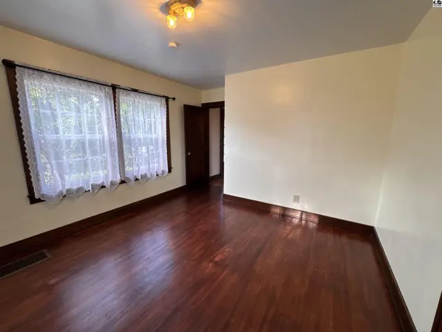 Spacious room with dark hardwood floors, white lace curtains, and neutral walls.