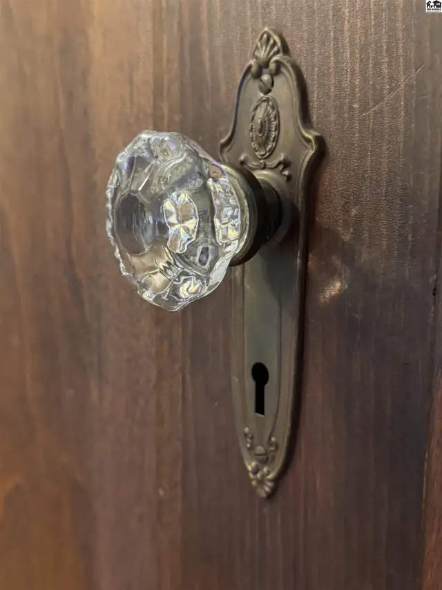 Antique brass doorknob with a faceted crystal knob on a dark wood door.