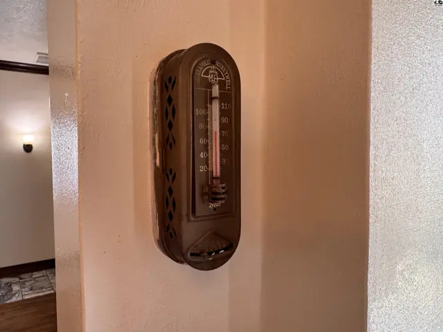 Vintage wall-mounted thermometer with a metal casing and visible mercury column.