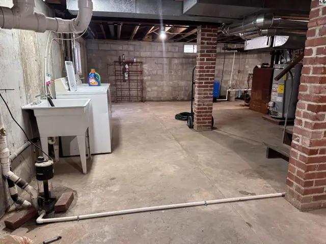 Unfinished basement with concrete floors, exposed pipes, laundry area, and brick accents.