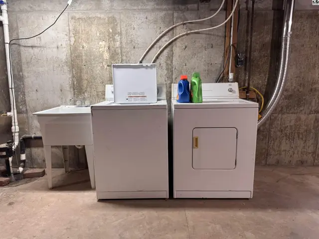 Laundry area with white washer, dryer, utility sink, and concrete walls.