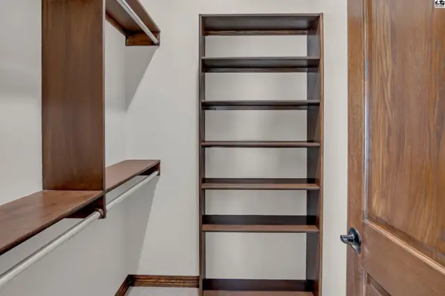 This closet features built-in shelving and a hanging rod with a wooden door.