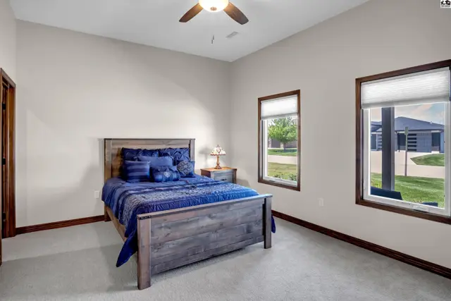 Spacious bedroom with a wooden bed frame, plush carpet, and large windows.