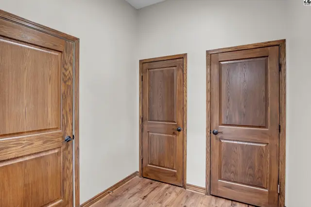 Three paneled wooden doors with dark hardware are set into a neutral wall above a wood-plank floor.