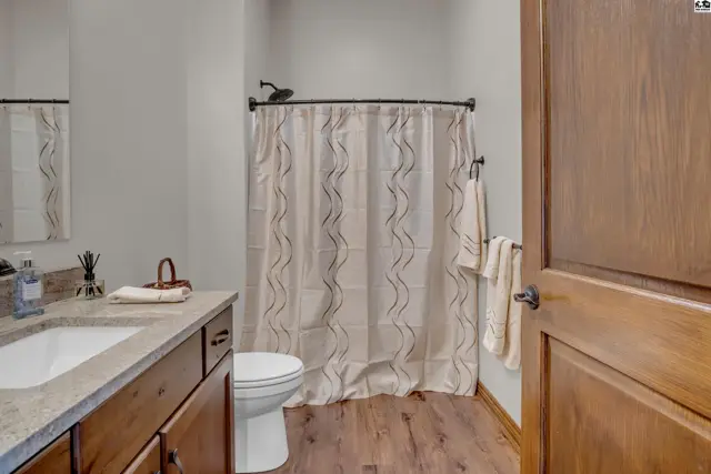 This bathroom features a vanity with a granite countertop, a toilet, and a shower with a patterned curtain.