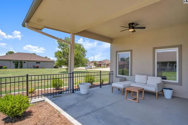 Covered patio with ceiling fan, concrete floor, and outdoor seating overlooks a fenced yard.