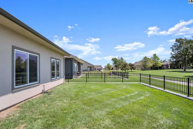 A fenced lawn with green grass extends from the side of a stucco house.