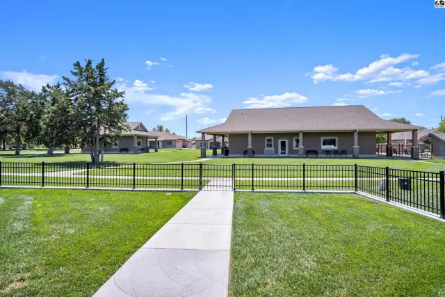 A paved walkway leads through a fenced lawn to a building with a covered porch.