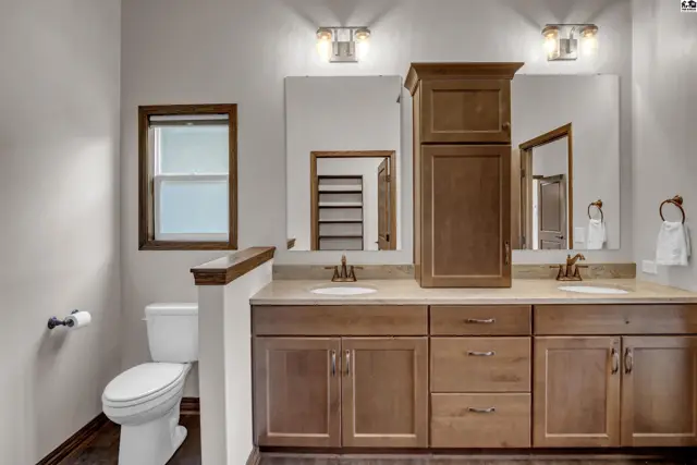 This bathroom features a double vanity with wood cabinetry, a large mirror, and a separate toilet area.