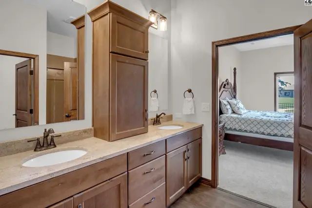 This bathroom features a double vanity with granite countertops and a tall wooden cabinet.