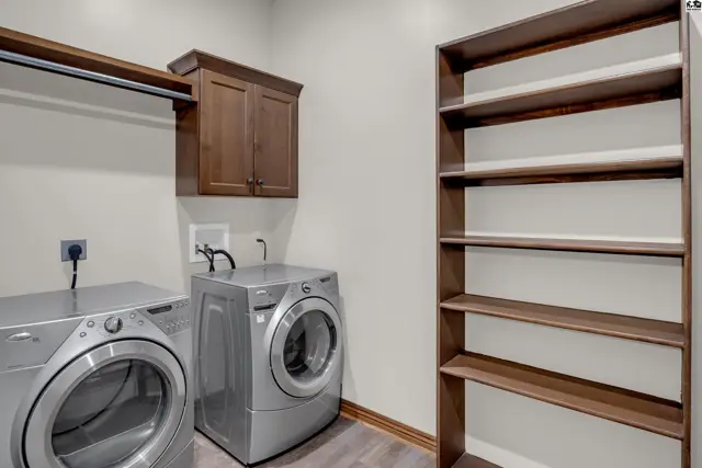 This laundry room features silver-toned appliances, a wooden cabinet, and a tall shelving unit.