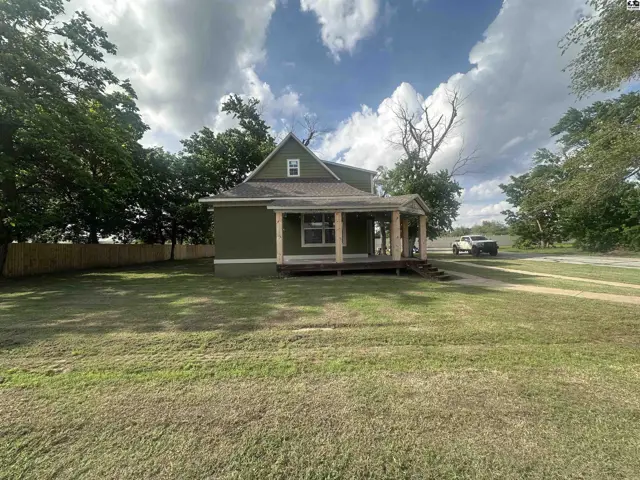 Green house with a covered front porch, wooden columns, and a large grassy yard.