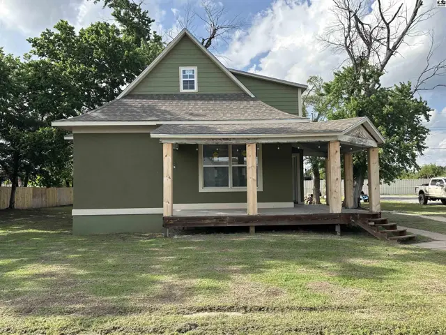 Green stucco house with a covered wooden porch and rustic beam supports.