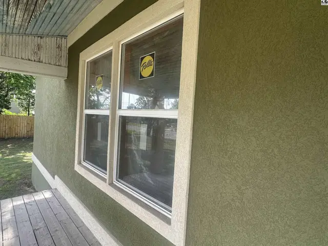 Exterior view of a green stucco house with white-trimmed windows and a wooden porch.