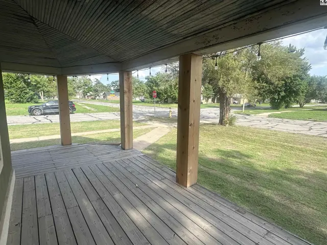 Covered wooden porch with natural wood columns and a corrugated metal ceiling overlooks a tree-lined street.
