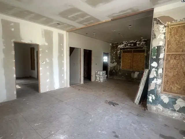 Interior renovation in progress with drywall, exposed studs, and boarded windows.