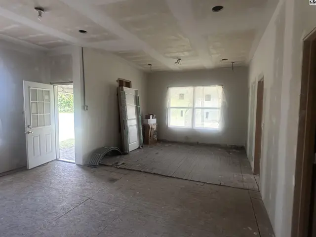 Spacious, unfinished living area with drywall, a large window, and an exterior door.