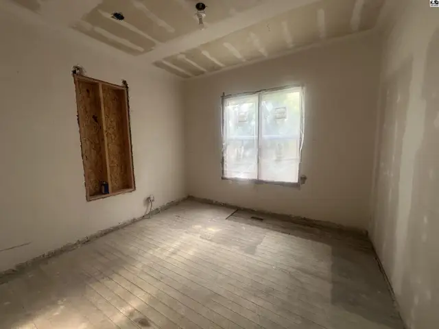 Unfinished room with exposed ceiling joists, drywall, and a window covered with plastic.