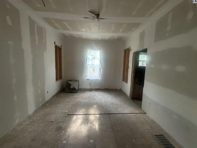 Unfinished living room with drywall, bare floors, and a ceiling fan, awaiting renovation.