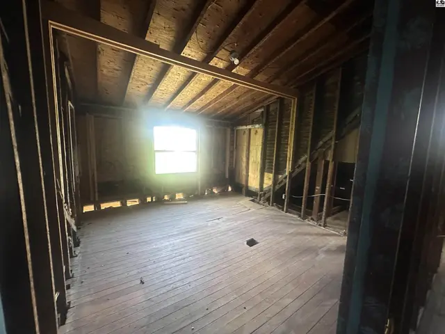Interior view of a room with exposed wooden beams, unfinished walls, and hardwood floors.